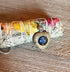 The Lapis Lazuli Spinner Pendant—featuring a blue jasper stone—rests on dried sage and petals, wrapped in white string atop textured wood, making this necklace the perfect calming fidget jewelry.