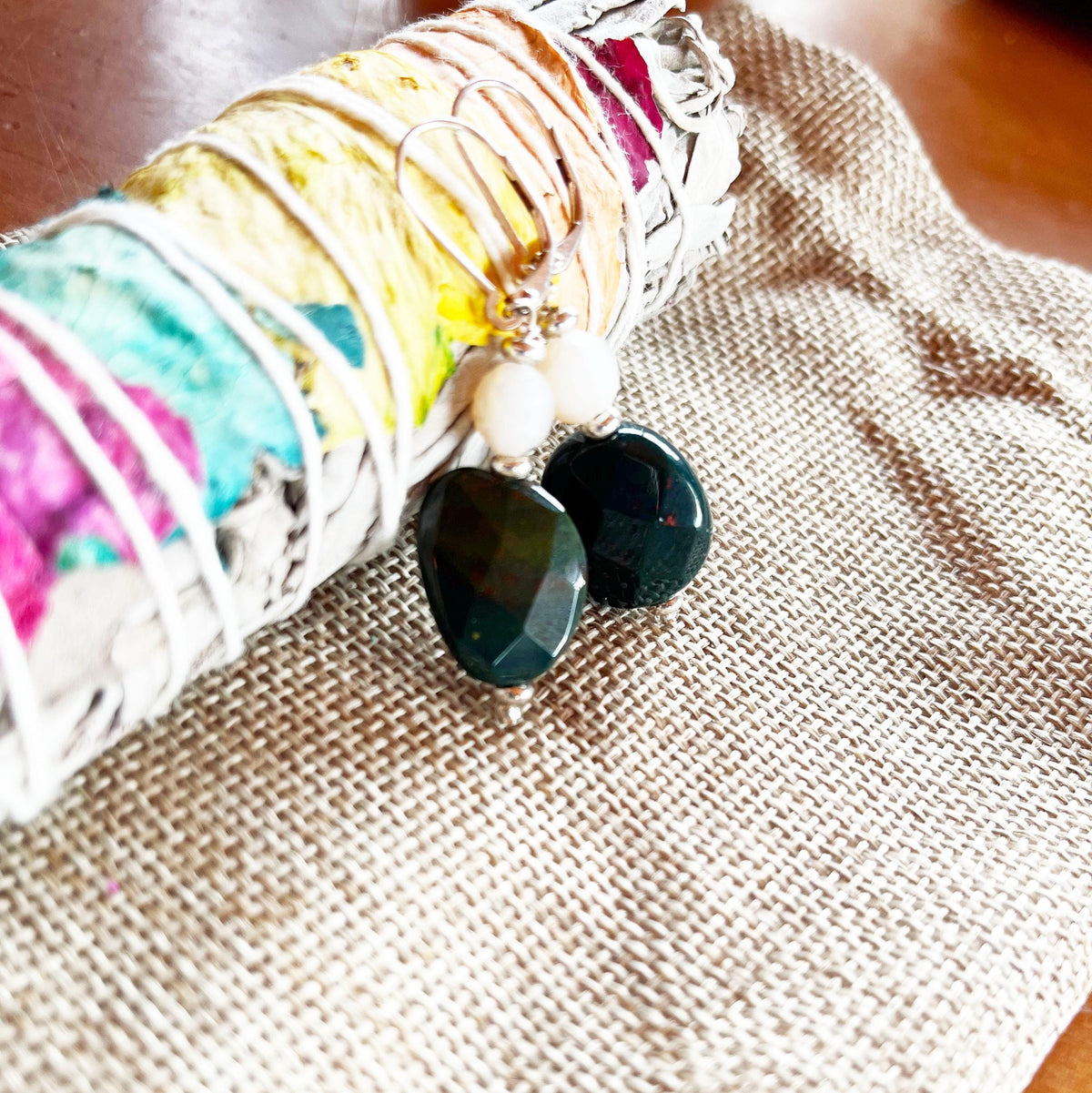The Teal Indian Agate Earrings, featuring a winter zen theme and minimalist faceted stone design, rest on burlap next to a colorful sage bundle, perfectly capturing serene elegance and seasonal charm.