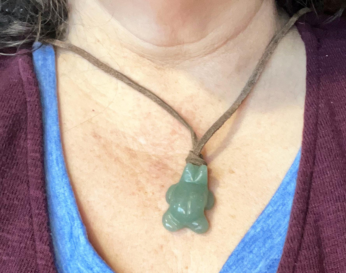 A person wears the Turtle Necklace Stone Primitive—a carved aventurine or African turquoise tortoise totem on an adjustable leather cord—over a blue shirt and maroon sweater.