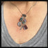 A close-up of a person wearing the Fancy Jasper Feather Pendant Necklace: Artisan Zen Jewelry, showcasing gemstone pendants in purple, green, and translucent hues against a light gray shirt.