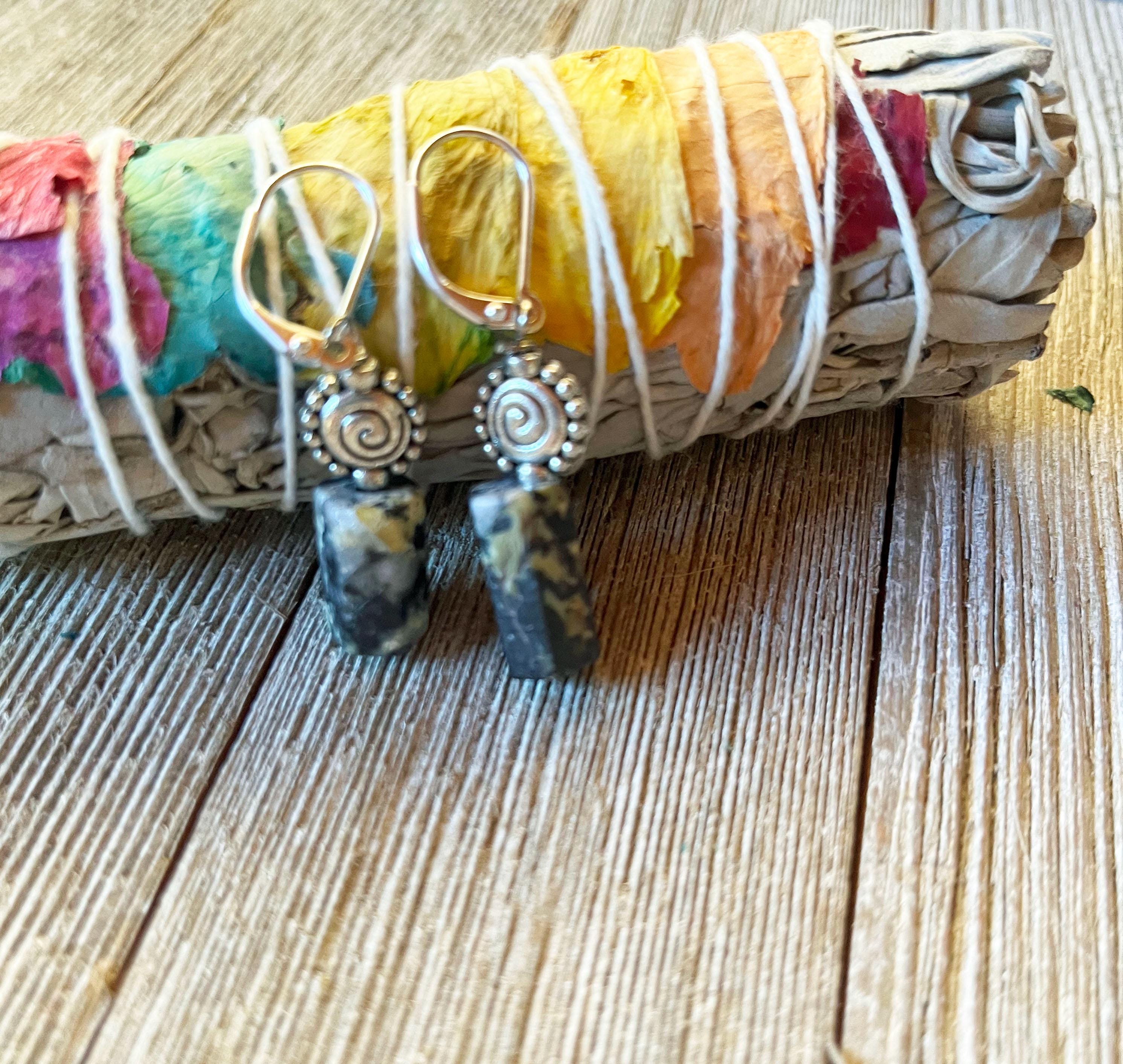 Swirling Ocean Jasper Earrings—Winter Theme Zen Minimalist Jewelry—feature black and yellow marbled stones with spiral silver hooks, shown beside a sage bundle tied with flower petals and white string on a wooden surface.
