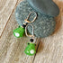 Handcrafted Glass Frog Earrings: Animal Lover Jewelry Gift featuring silver hooks and frog charms, elegantly displayed on stacked gray stones atop rustic wood—a delightful accessory for any animal jewelry enthusiast.