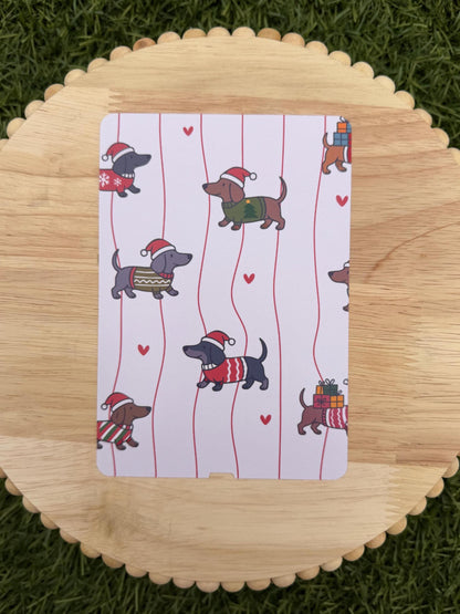 May include: A white card with a repeating pattern of dachshunds wearing Santa hats and sweaters, set against red vertical stripes and small red hearts. The dachshunds are in various colors and poses.