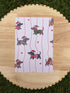 May include: A white card with a repeating pattern of dachshunds wearing Santa hats and sweaters, set against red vertical stripes and small red hearts. The dachshunds are in various colors and poses.