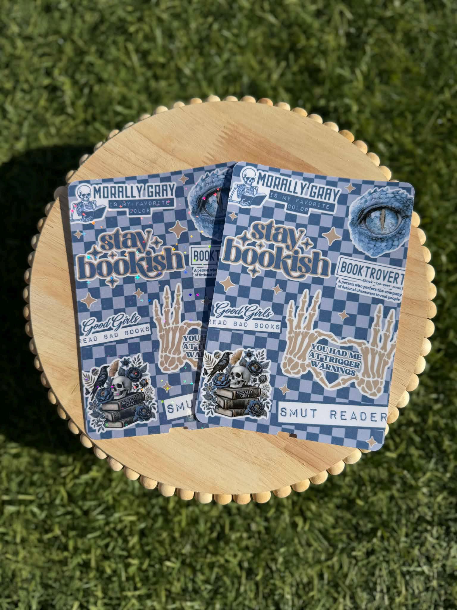 May include: Two stickers with a blue and white checkered background. The stickers have text that says &amp;quot;MORALLY GRAY&amp;quot;, &amp;quot;stay bookish&amp;quot;, &amp;quot;Good Girls Read Bad Books&amp;quot;, and &amp;quot;SMUT READER&amp;quot;. Other graphics include a skull, a skeleton hand, and an eye.