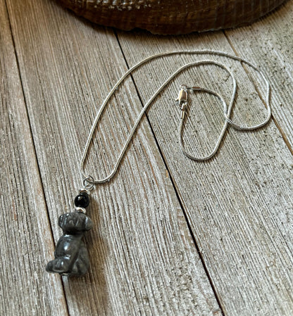 The Carved Obsidian Dog Necklace - Color Change Bead, Pet Memorial features a small dog pendant and a color-changing bead, displayed on a rustic wooden surface.