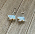 Handcrafted Stone White Bear Earrings shimmer like the northern lights with iridescent bear charms and clear beads on sterling silver lever backs, beautifully displayed on a rustic wooden surface.