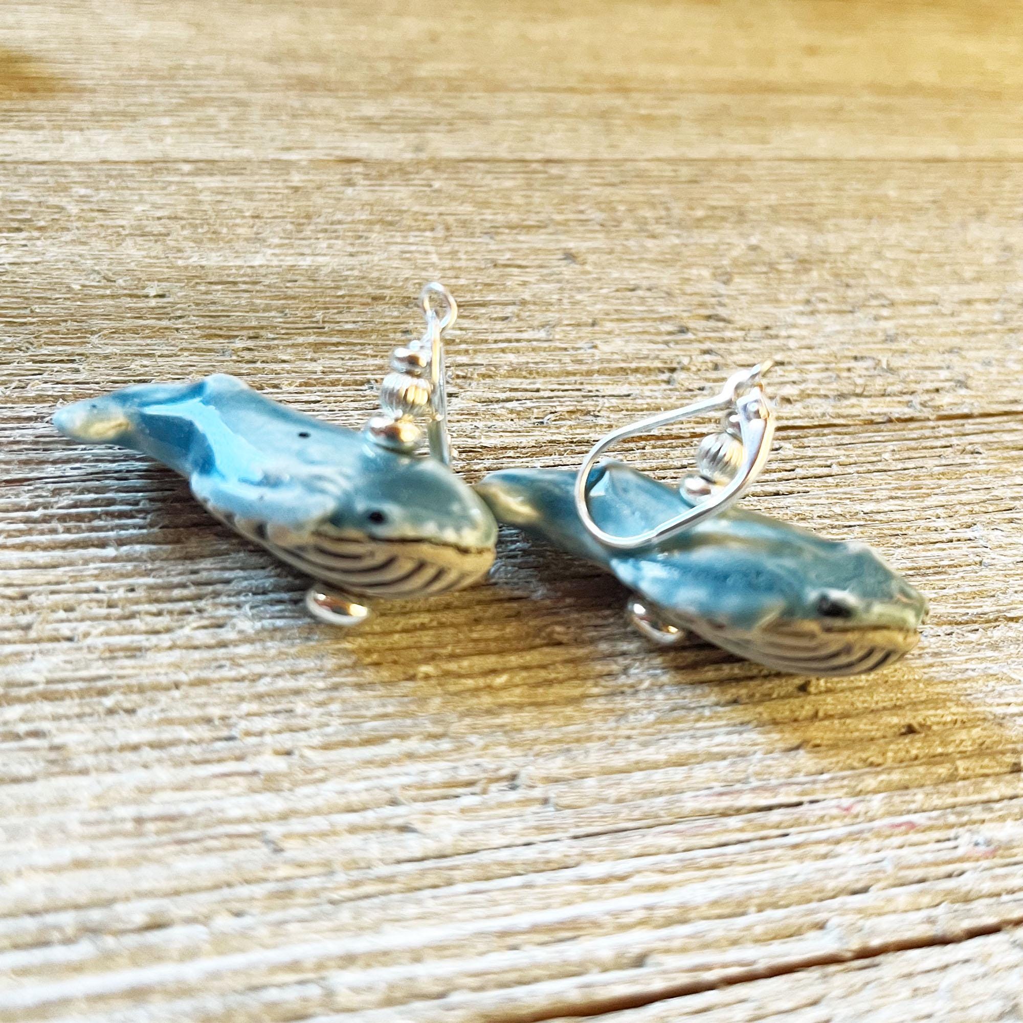 Hand-Painted Blue Whale Dangle Earrings with detailed fins and undersides rest on a textured wooden surface—perfect ocean-themed jewelry and a thoughtful gift for nature lovers.