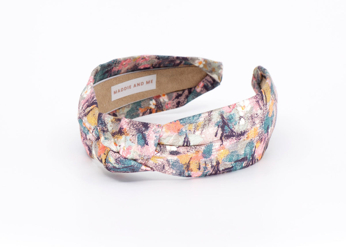 May include: A knotted headband with a colorful abstract pattern. The fabric features a mix of pink, blue, yellow, and orange brushstrokes on a neutral background. The headband has a label that says &amp;quot;MADDIE AND ME&amp;quot;.