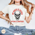 May include: Ivory-colored t-shirt with a skull graphic and the text "MY ANGER IS SACRED" and "MY RAGE IS RIGHTEOUS" in red. The skull has a menacing expression. The shirt is a casual wear item.