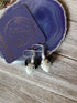Handcrafted Glass Bull Head Earrings, featuring small white charms and pearls, displayed on a purple agate slice beside a card with gold celestial designs and LINADORN HANDCRAFTED JEWELS—an ideal animal lover jewelry gift.