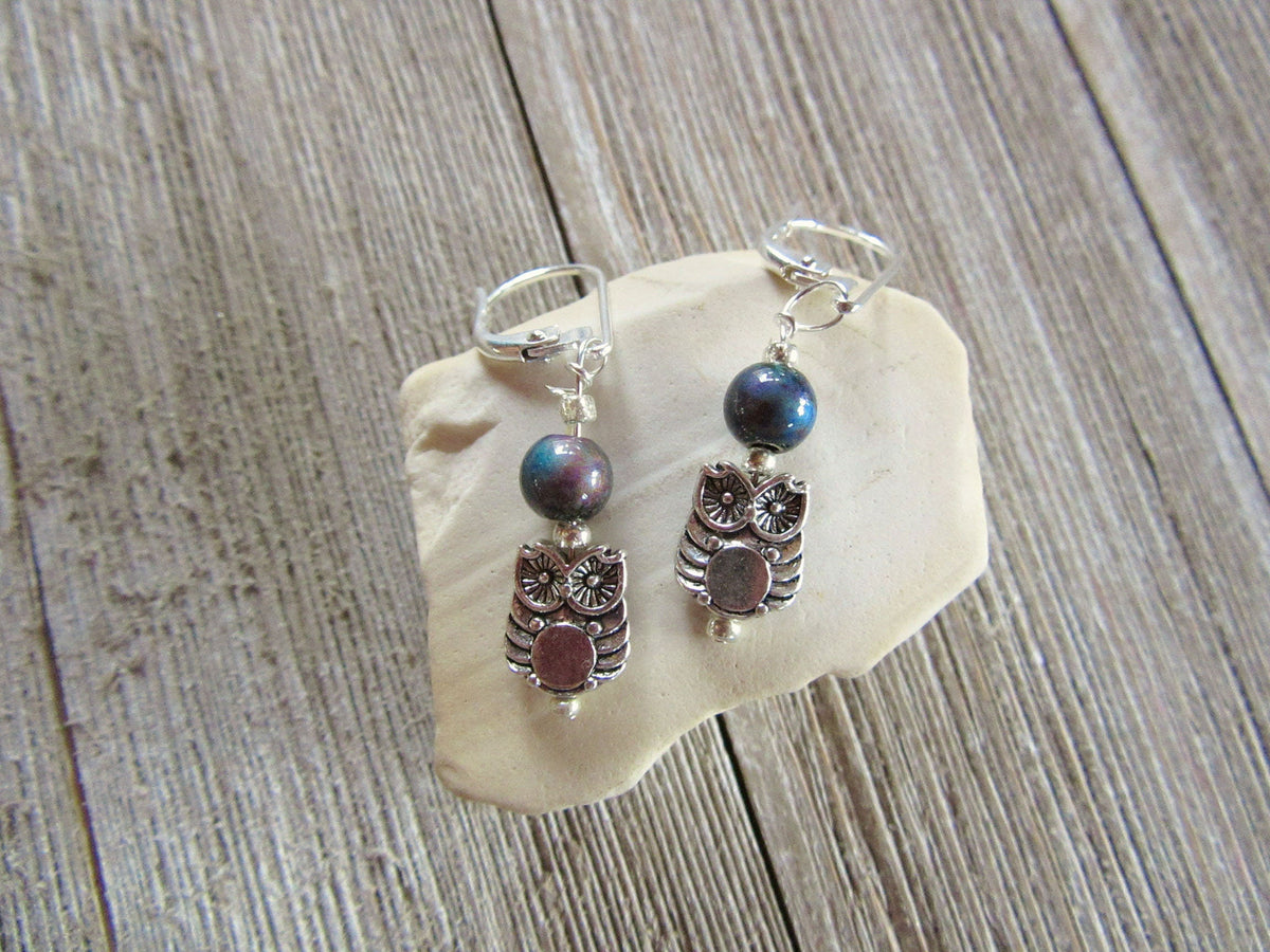 Two sterling silver Owl Earrings with fun, color-changing mood beads are displayed on a light stone atop rustic wood—unique "Owl Earrings: Tiny and Fun Color Changing Mood Bead," perfect for any collection.