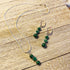 The Green Malachite Heart Jewelry Set features a Spring Dangle Necklace with three green striped beads in a row and matching earrings with two beads each—an elegant handcrafted set displayed on light wood, perfect for any occasion.