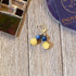 Handmade Citrine Sodalite Spring Earrings: Geometric Circles Spheres, featuring yellow and blue beads, are shown on a wooden surface with a stained glass piece and an ENLIVEN DESIGNS TO card. Ideal for lovers of unique spring or geometric earrings.