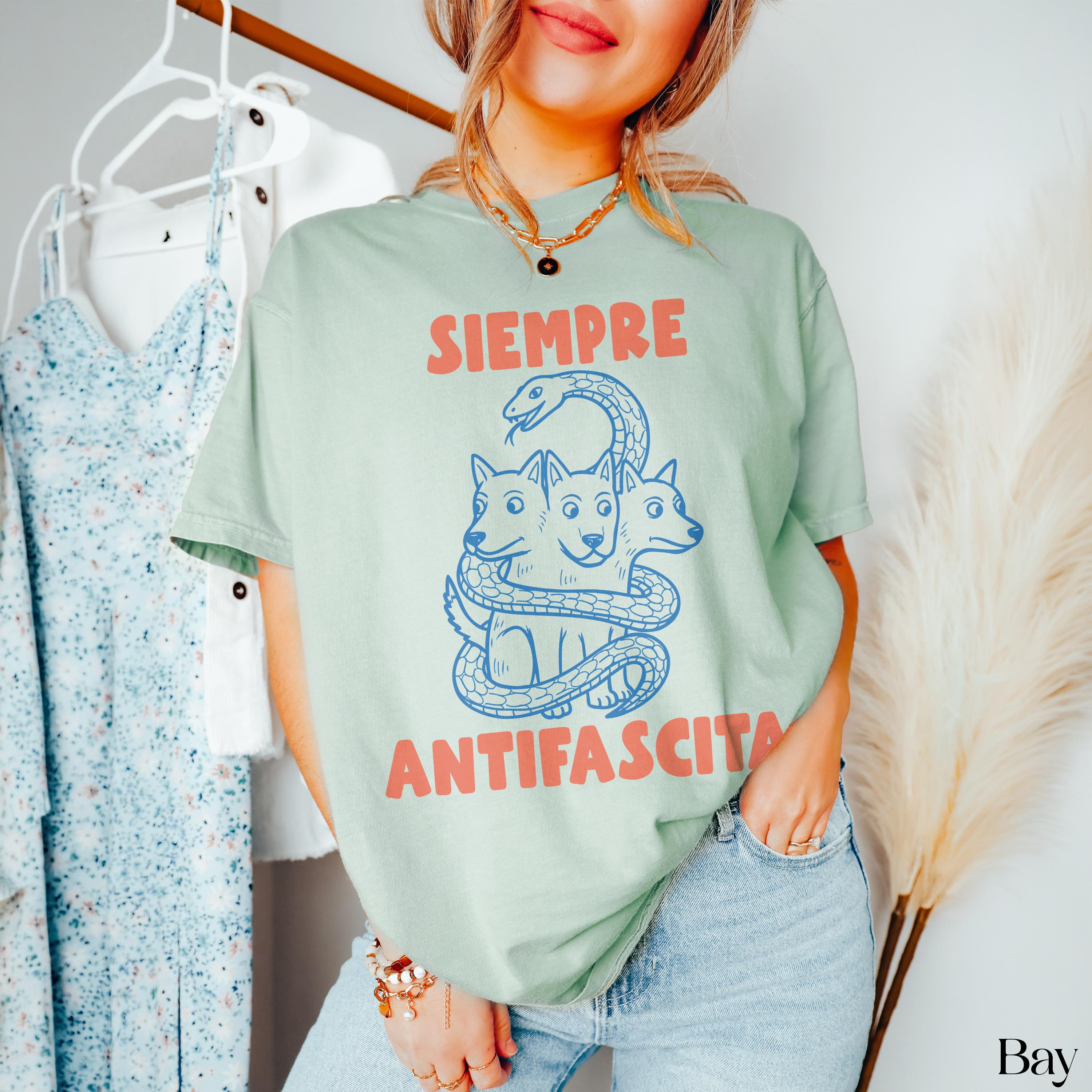 Mint t-shirt with a blue graphic of a three-headed dog wrapped in a snake, text &amp;quot;SIEMPRE ANTIFASCISTA&amp;quot;.