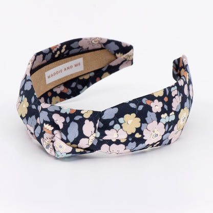 A floral-patterned headband with a knotted design. The headband has a label that says &amp;quot;MADDIE AND ME&amp;quot;.