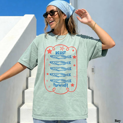 Sage green t-shirt with a graphic of five fish swimming left and text &amp;quot;Resist Turn Left.&amp;quot;