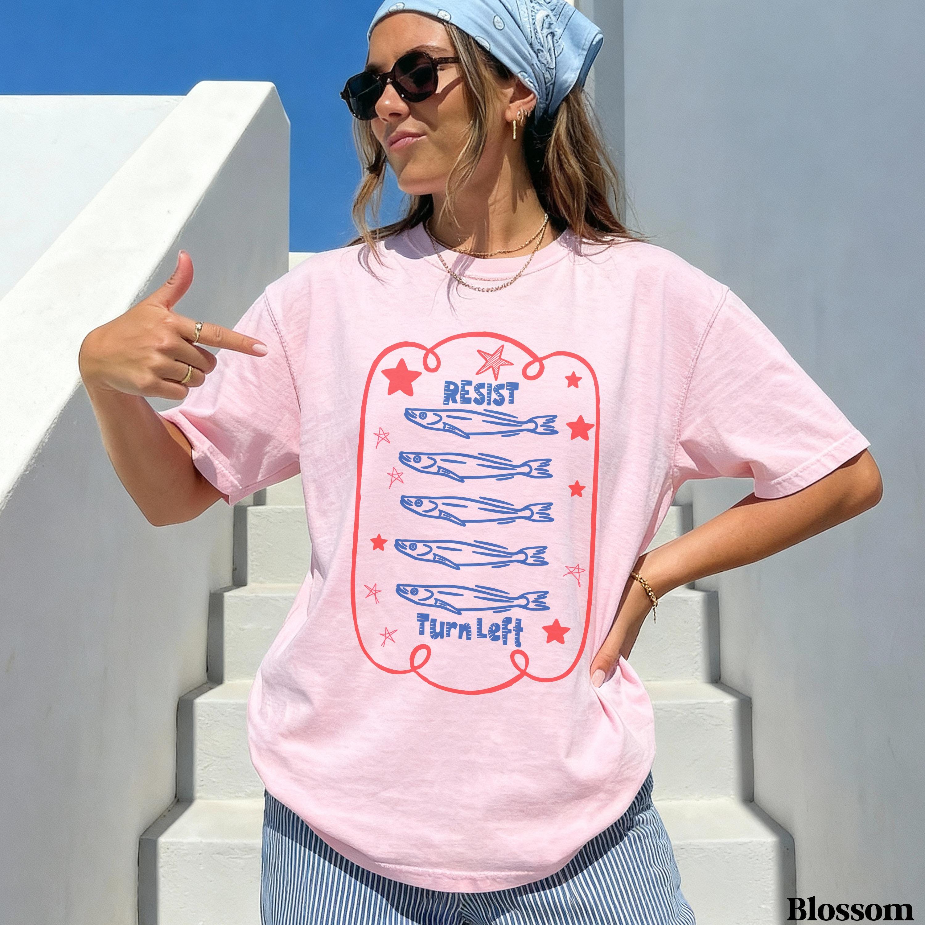 Pink t-shirt with &amp;quot;Resist&amp;quot; and cartoon fish above &amp;quot;Turn Left&amp;quot;.