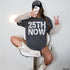 Woman in charcoal t-shirt with "25TH NOW" graphic and white cowboy boots.