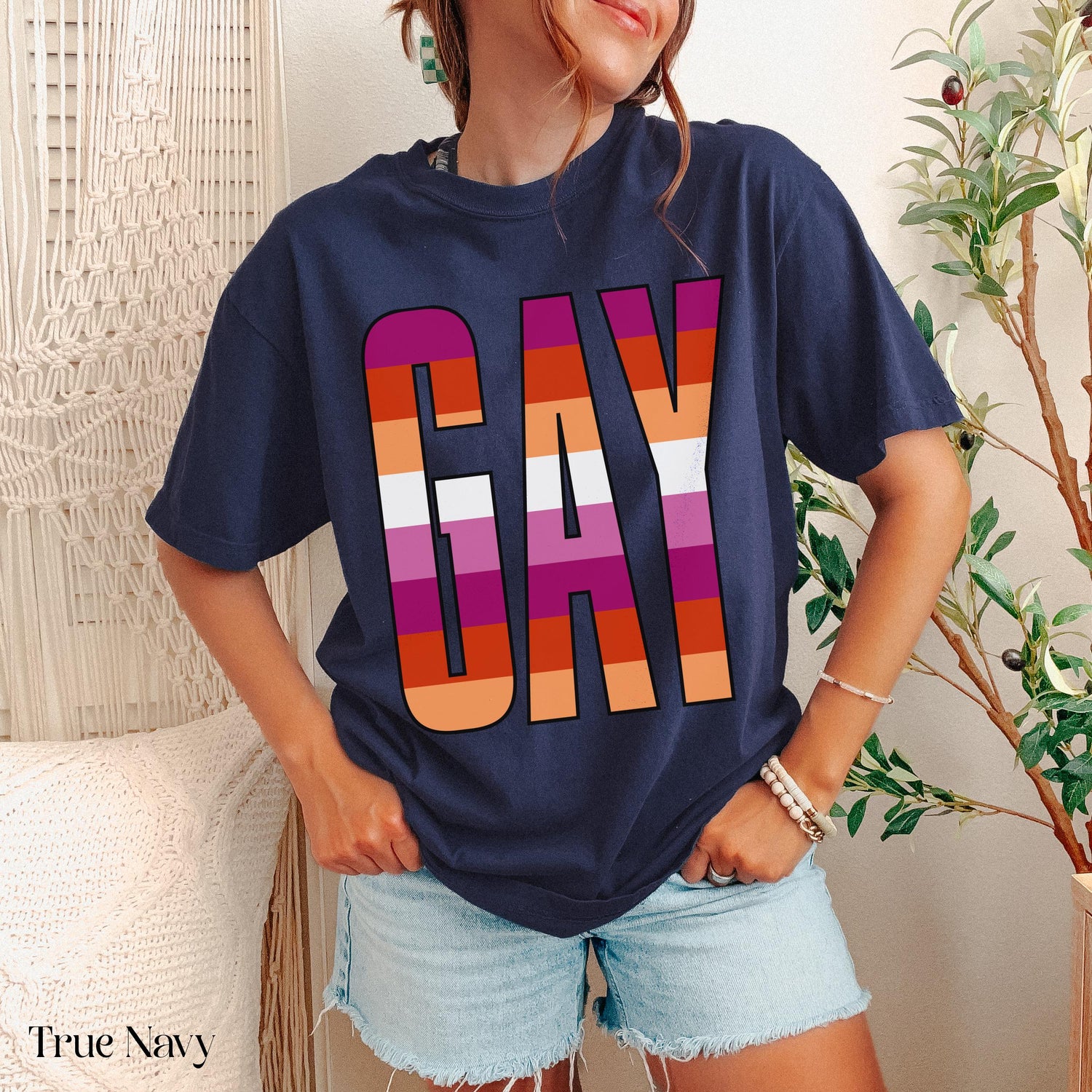 Woman wearing navy t-shirt with &amp;quot;GAY&amp;quot; in rainbow stripes, holding hands at waist.