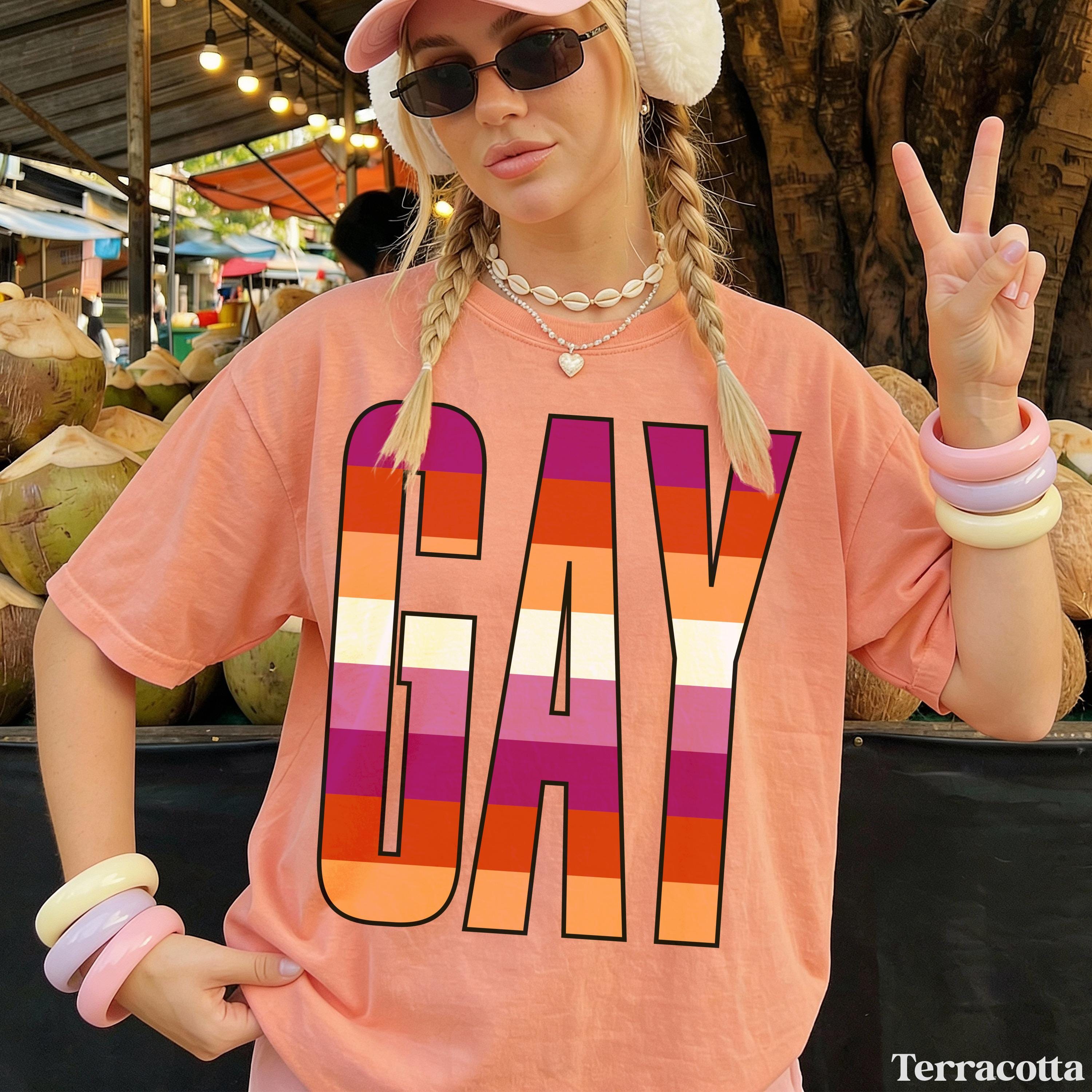 Woman wearing pink shirt with &amp;quot;GAY&amp;quot; in pride flag colors and peace sign.