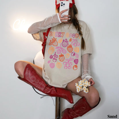 Woman in beige t-shirt with &amp;quot;Berry Good&amp;quot; text and berry illustrations, wearing red boots.