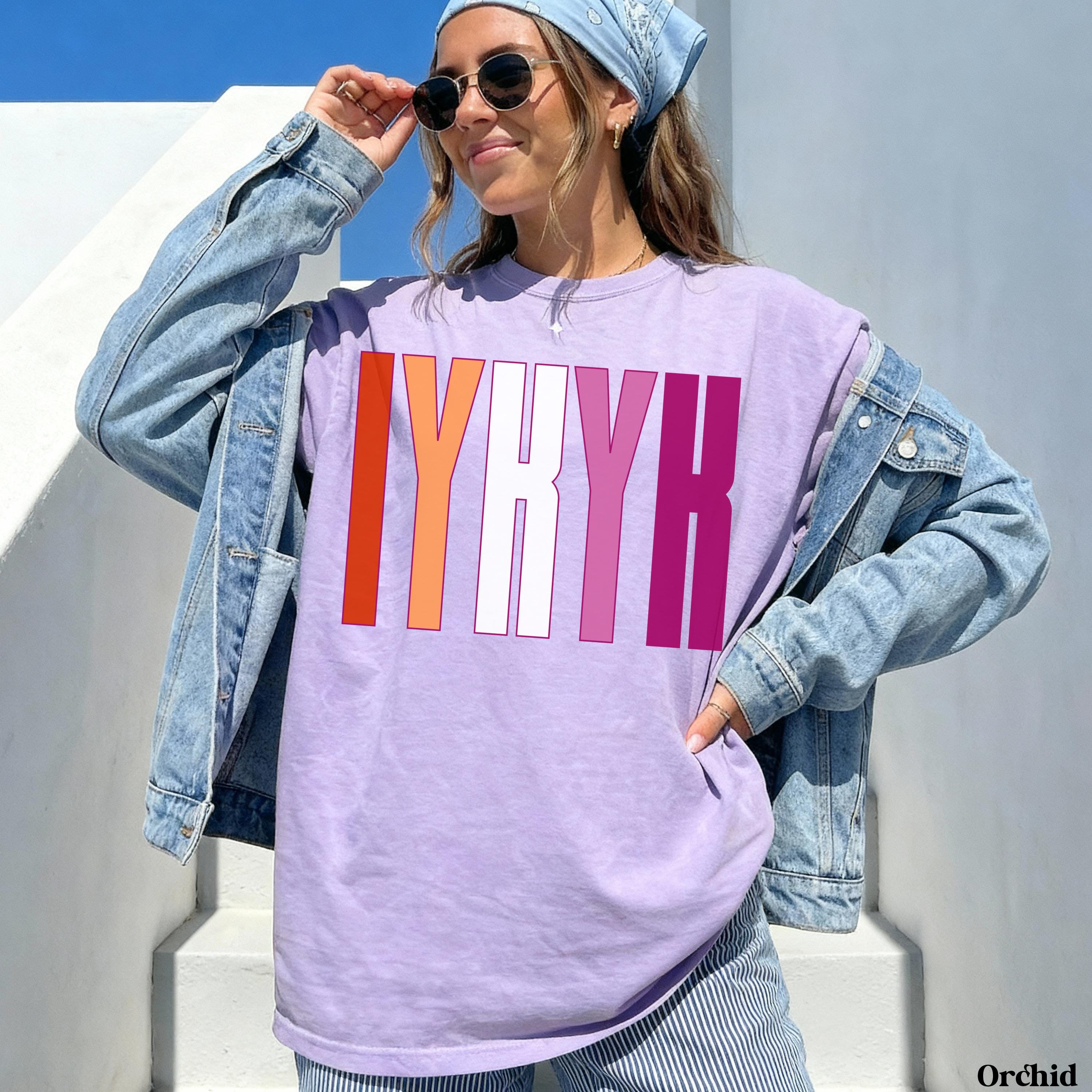 Woman wearing a purple t-shirt with &amp;quot;IYKYK&amp;quot; in pink and orange stripes.