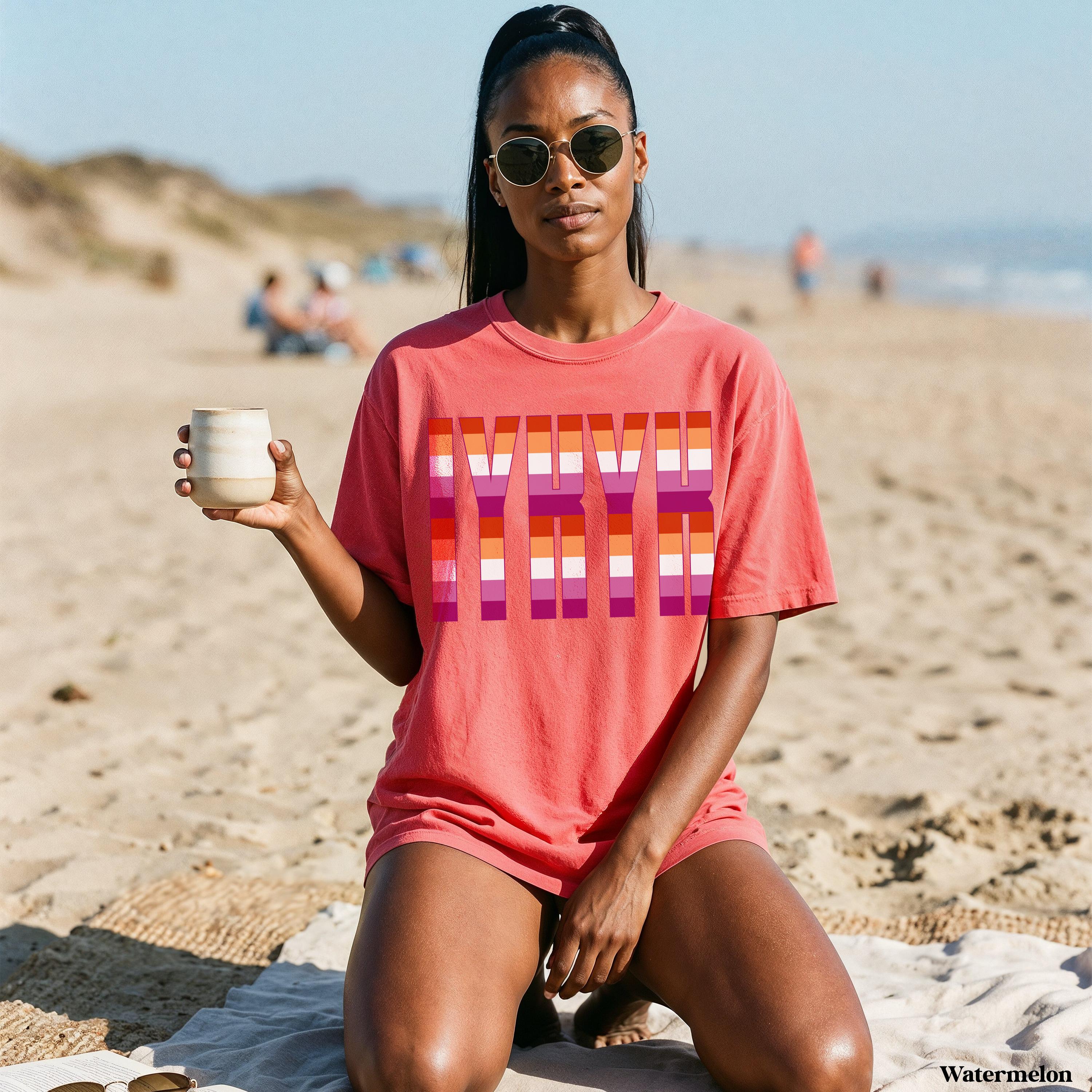 Woman in coral t-shirt with &amp;quot;LOVE&amp;quot; in rainbow stripes, holding a mug on beach