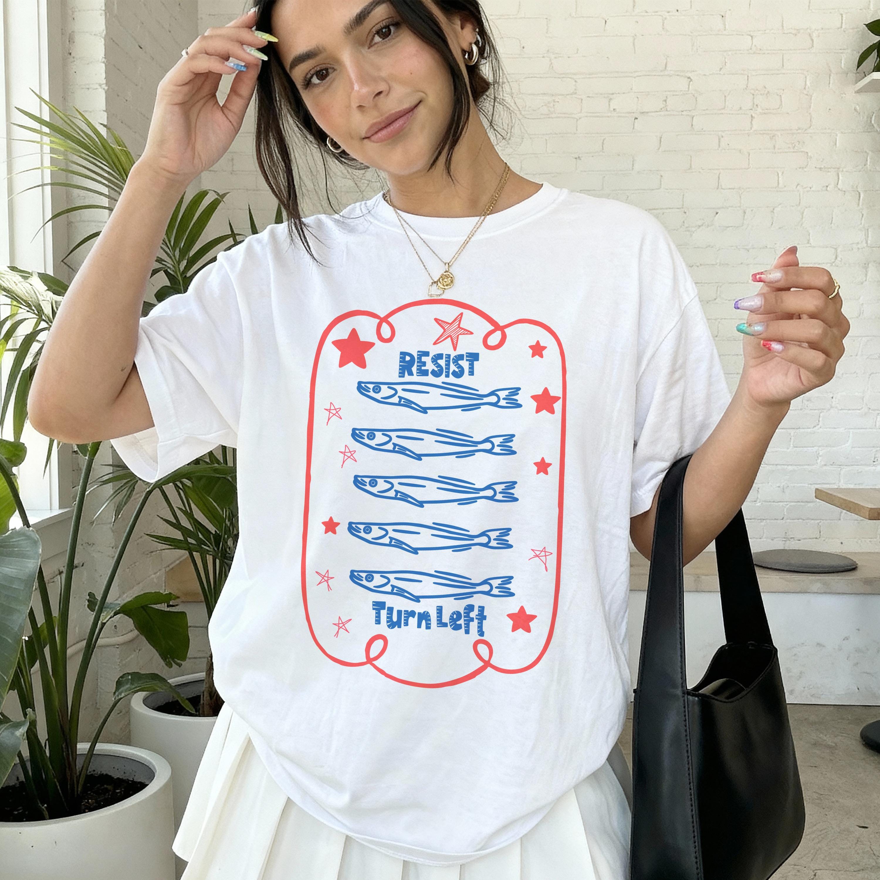 White t-shirt with blue fish graphic and &amp;quot;RESIST&amp;quot; and &amp;quot;TURN LEFT&amp;quot; text.