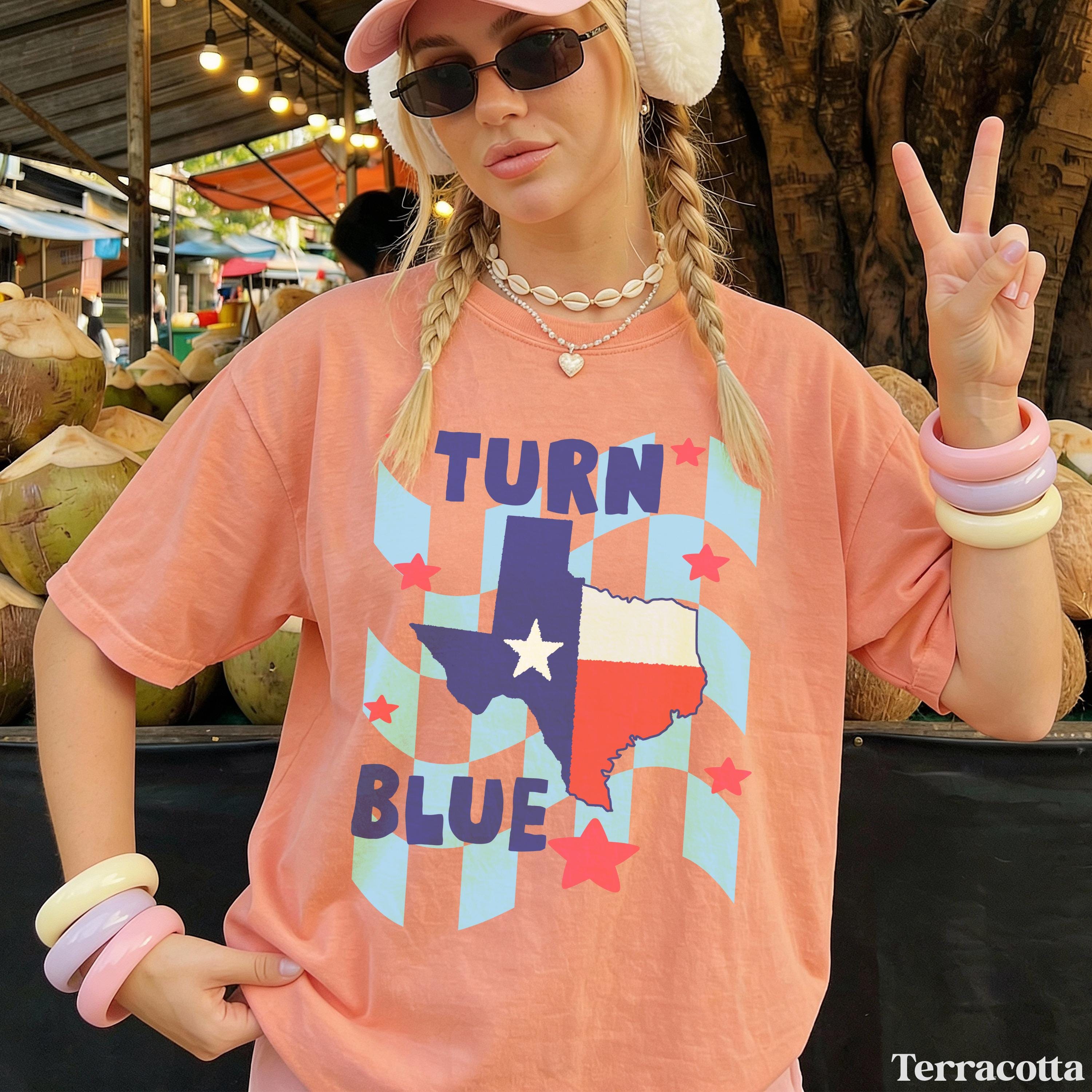 Woman wearing peach t-shirt with &amp;quot;Turn Blue Texas&amp;quot; graphic and peace sign.