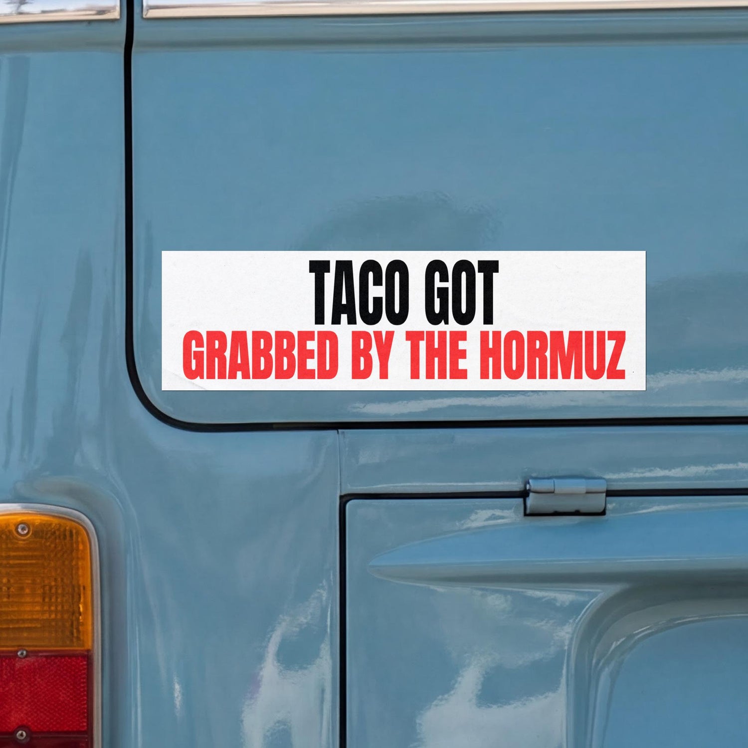 Bumper sticker on blue vehicle reads &amp;quot;TACO GOT GRABBED BY THE HORMUZ&amp;quot;.