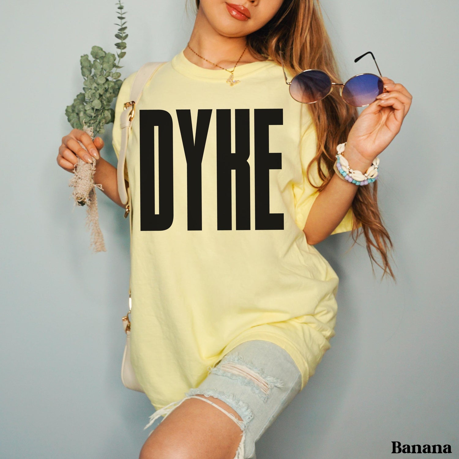 Light yellow t-shirt with &amp;quot;DYKE&amp;quot; in large black letters, held by a person wearing denim shorts.
