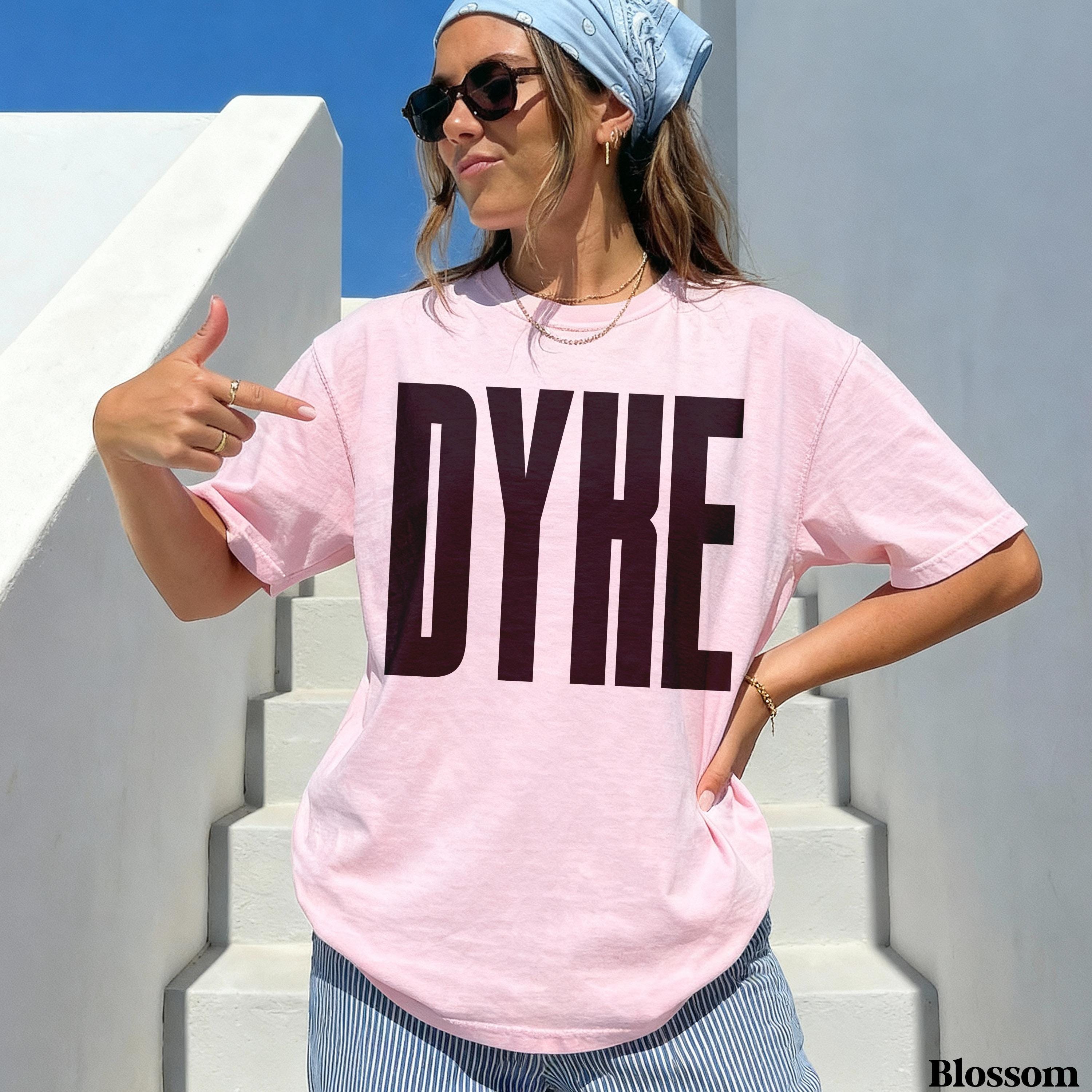Woman wearing pink t-shirt with bold black &amp;quot;DYKE&amp;quot; text, pointing at herself.