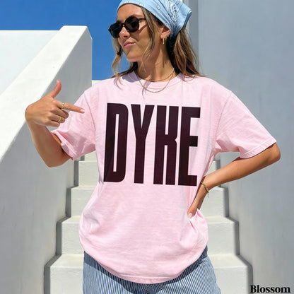 Woman wearing pink t-shirt with bold black &amp;quot;DYKE&amp;quot; text, pointing at herself.
