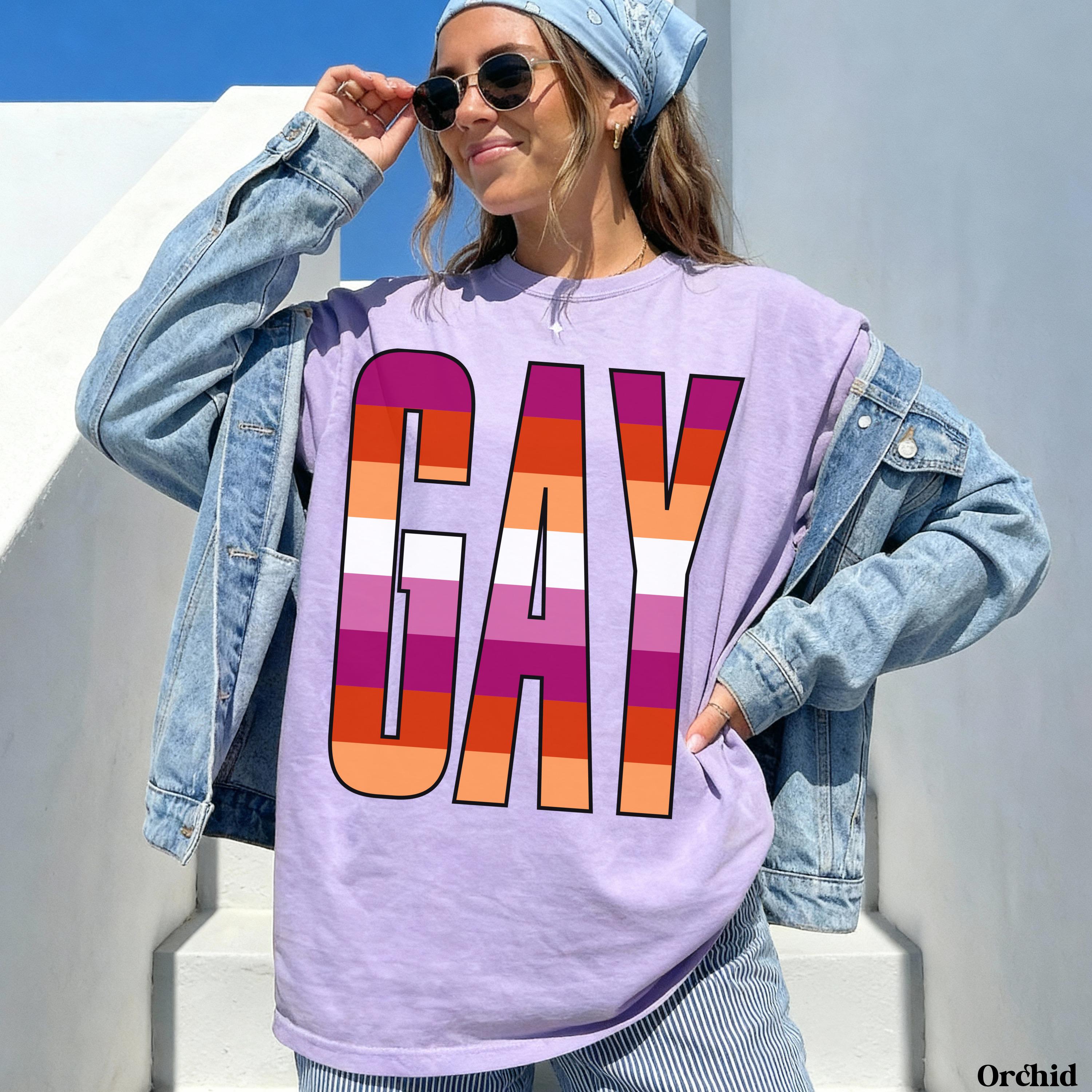Woman wearing a lavender t-shirt with &amp;quot;GAY&amp;quot; in rainbow stripes.