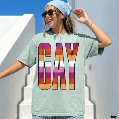 Woman wearing a pale green t-shirt with &amp;quot;GAY&amp;quot; in rainbow stripes.