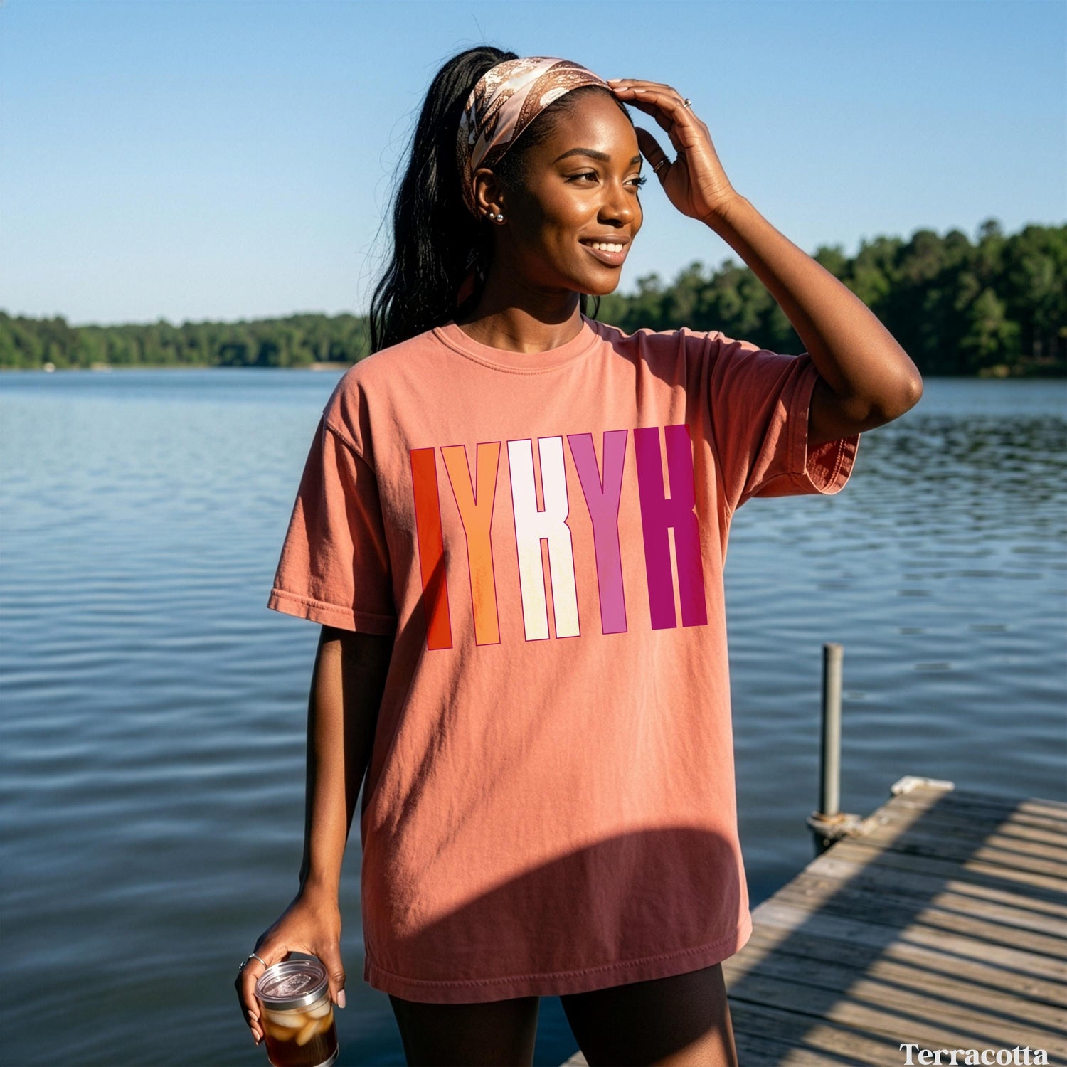 Woman wearing salmon t-shirt with &amp;quot;IYKYK&amp;quot; in gradient lettering, holding a drink.