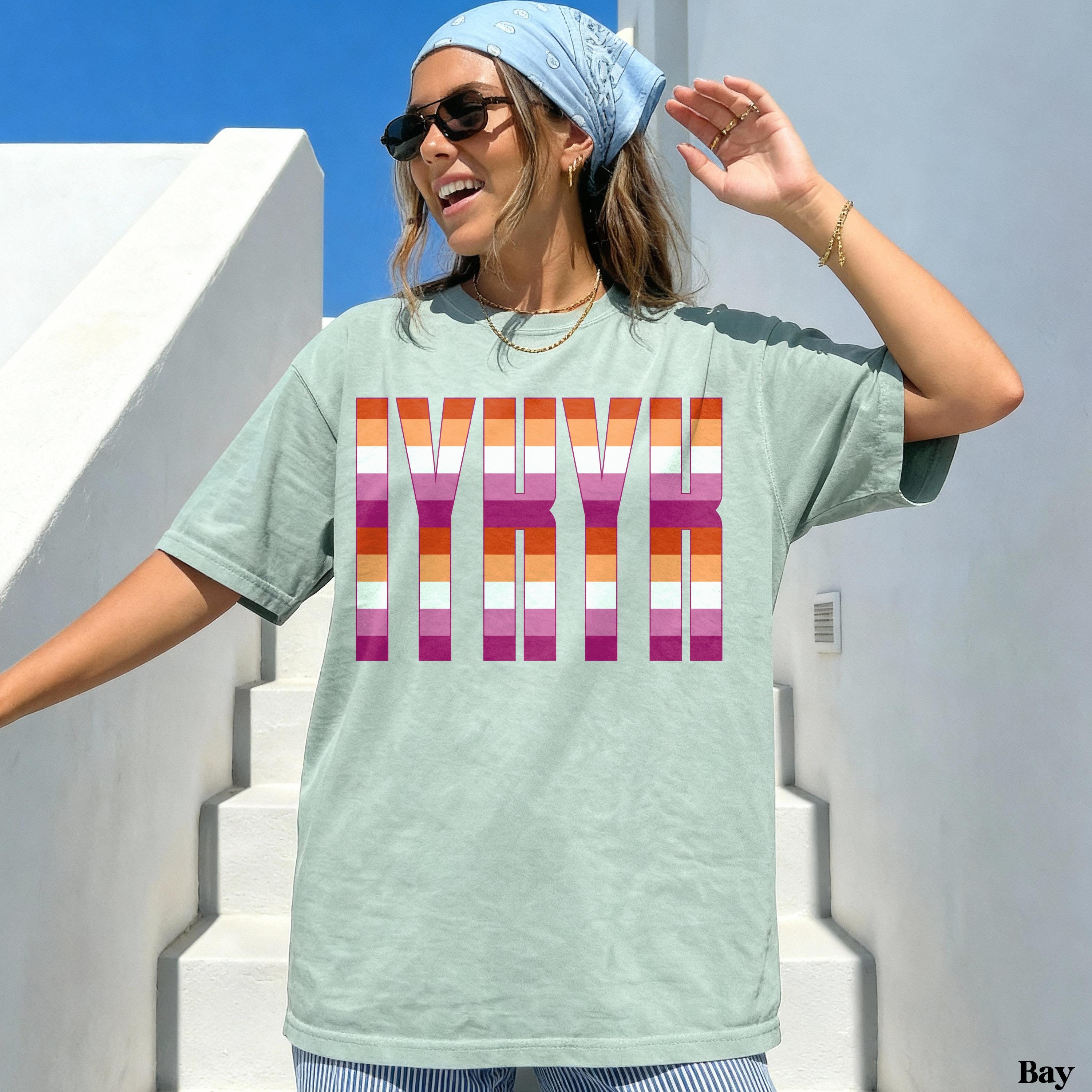 Woman wearing a light green t-shirt with LGBTQ+ pride flag stripes spelling &amp;quot;IYKYK&amp;quot;.