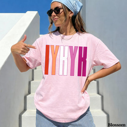 Pink t-shirt with &amp;quot;IYKYK&amp;quot; in lesbian flag colors, woman pointing.