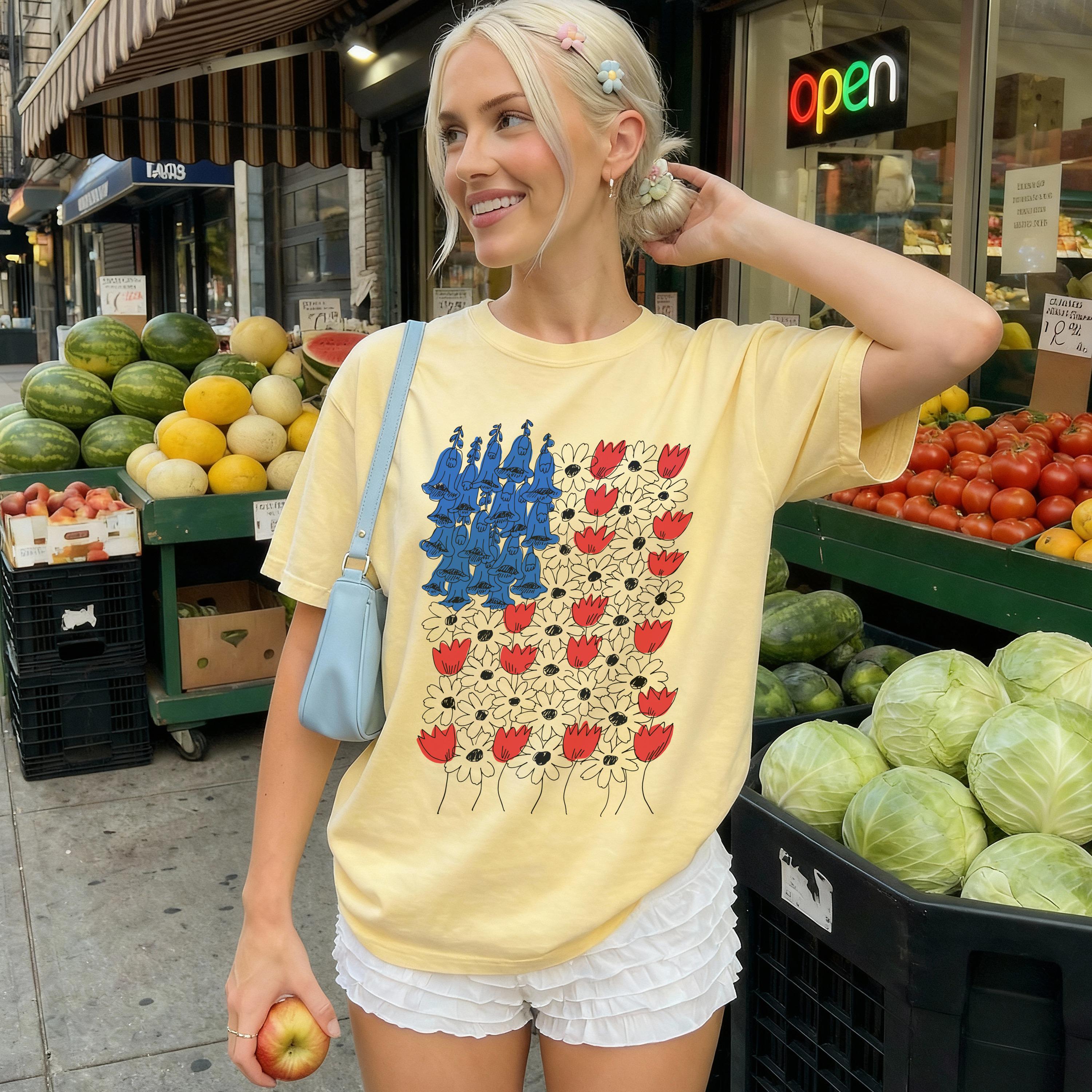 Woman wearing yellow graphic t-shirt with red flowers and blue figures, holding apple.