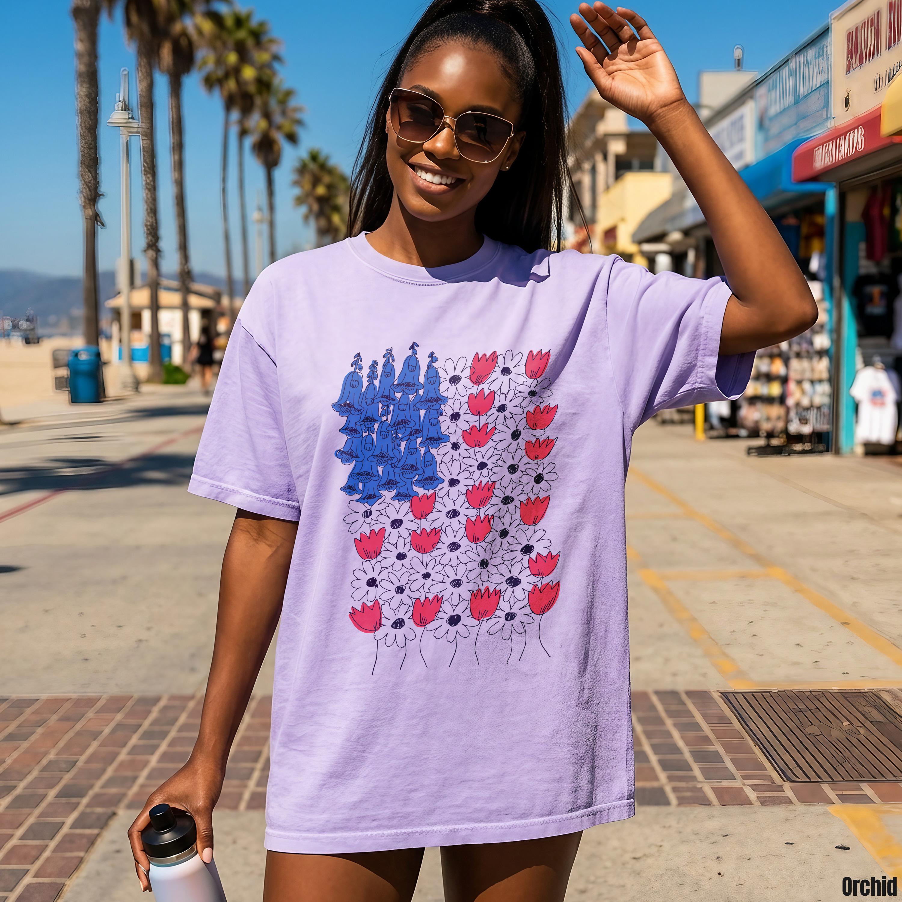 Purple t-shirt with abstract US flag design featuring red flowers and blue figures.