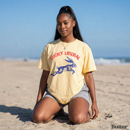 Woman kneeling on sand wearing yellow &amp;quot;Lucky Liberal&amp;quot; t-shirt with rabbit graphic.