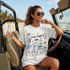 Woman in white t-shirt with "Trans People Live Dolce Vita" graphic, holding soda.