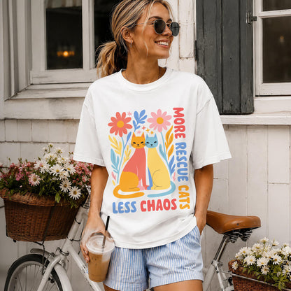 Woman wearing a white t-shirt with colorful cats and flowers, saying &amp;quot;More Cats Less Chaos&amp;quot;.