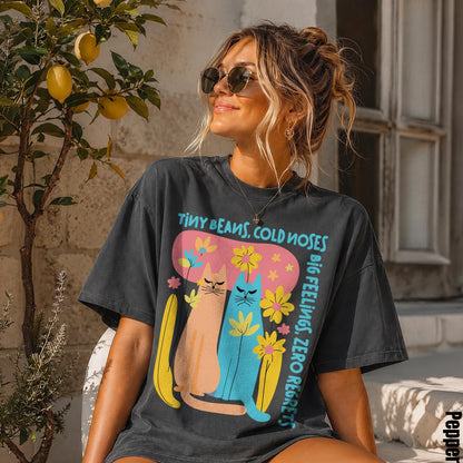 Woman in dark t-shirt with cats and flowers graphic, reads &amp;quot;Tiny Beans, Cold Noses&amp;quot;