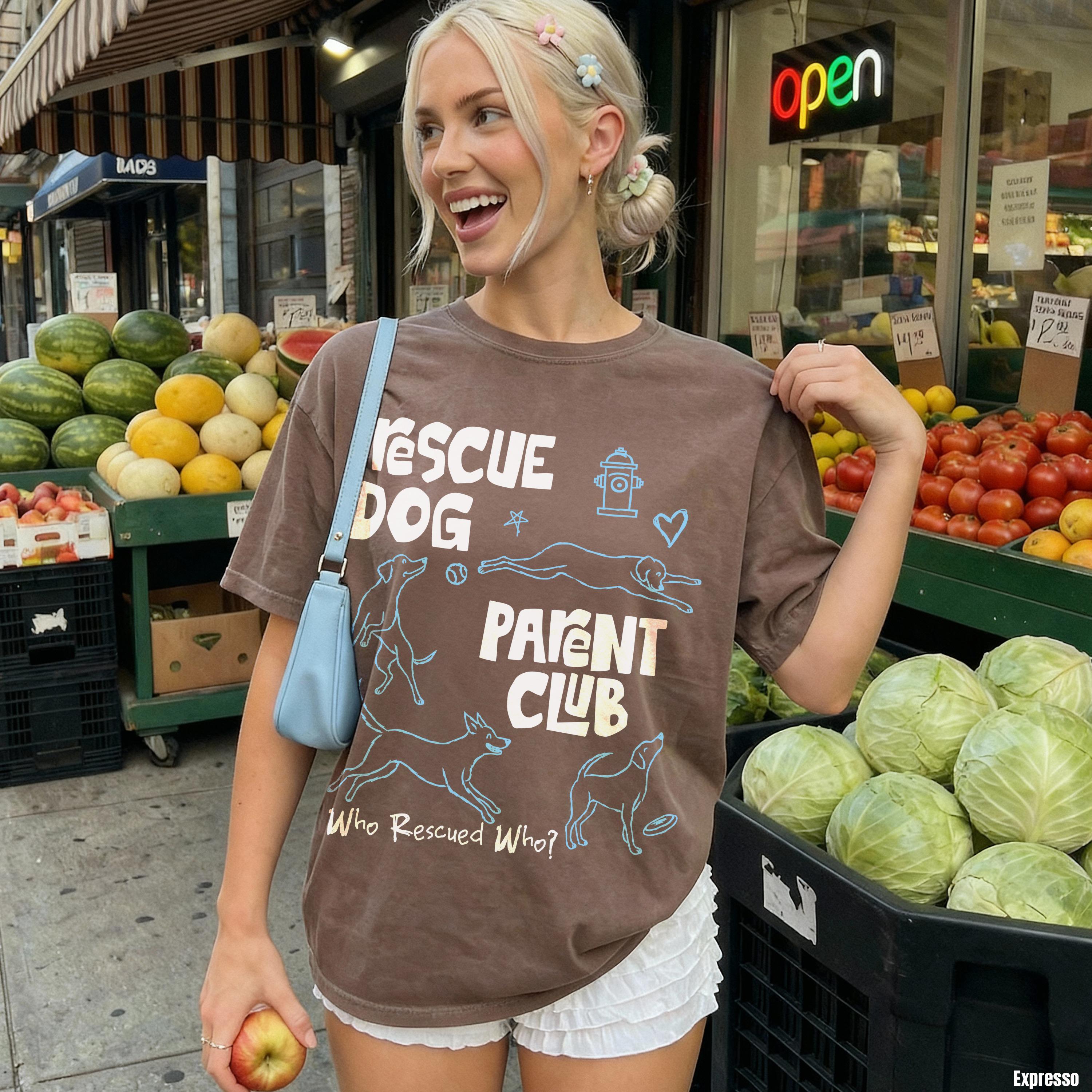 Woman in Rescue Dog Parent Club t-shirt holding apple, with produce stand behind her.
