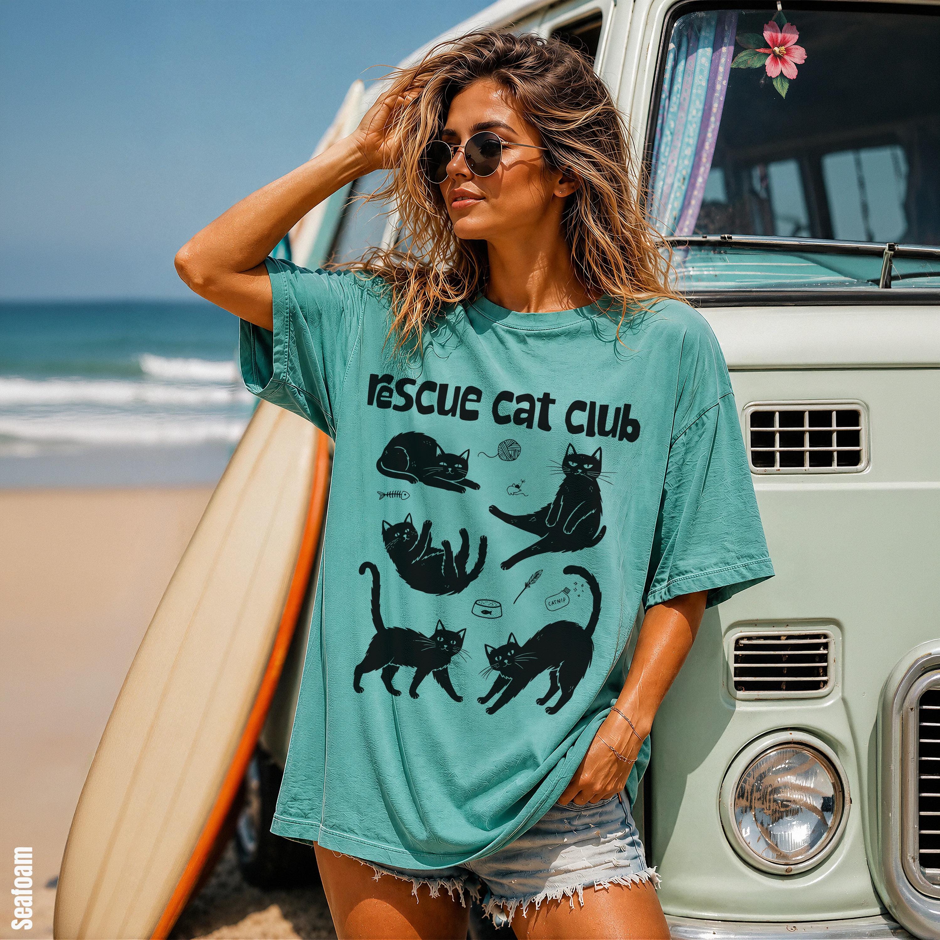 Woman wearing teal &amp;quot;rescue cat club&amp;quot; t-shirt stands by a vintage van.