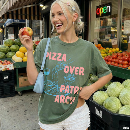 Green t-shirt with &amp;quot;Pizza Over Patriarchy&amp;quot; graphic, holding an apple at a fruit stand.