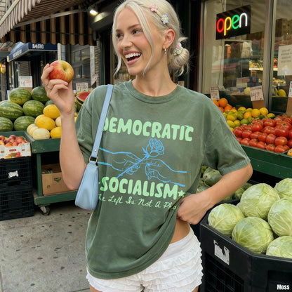 Woman wearing green t-shirt with &amp;quot;Democratic Socialism&amp;quot; text, holding an apple by fruit stand.