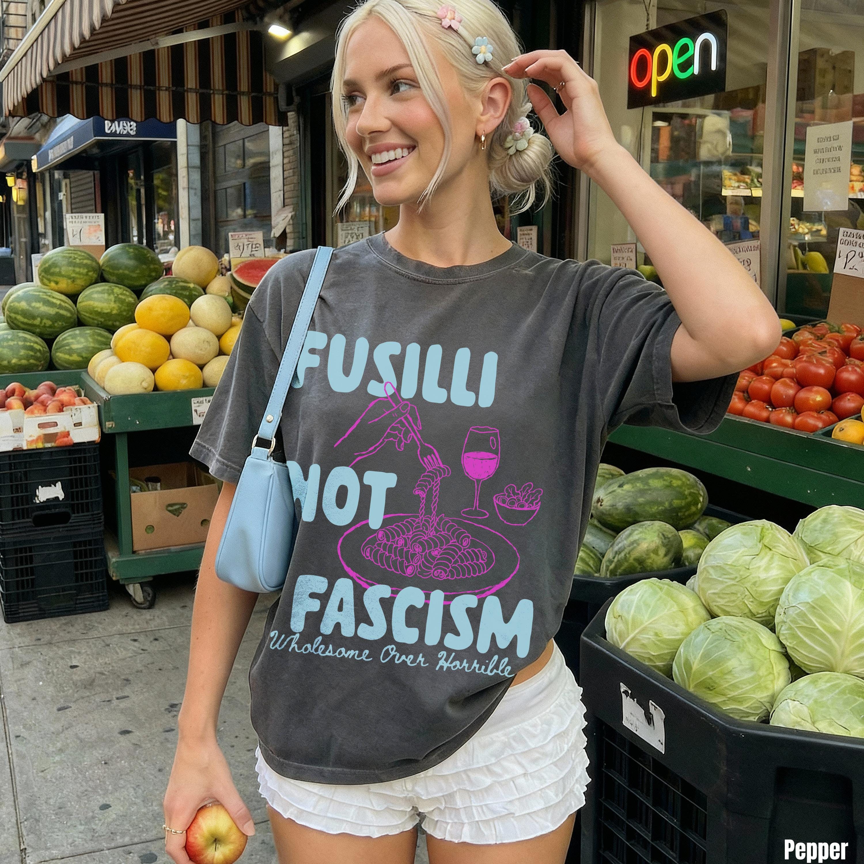 Woman in a dark gray t-shirt with &amp;quot;Fusilli Not Fascism&amp;quot; text and a blue purse.